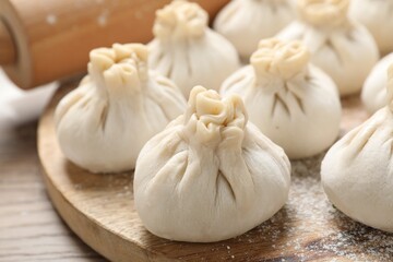 Uncooked khinkalis (dumplings) and rolling pin on wooden table, closeup