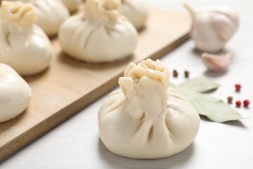 Uncooked khinkalis (dumplings) and spices on white wooden table, closeup