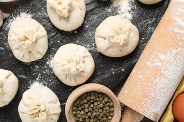 Uncooked khinkalis (dumplings), flour, spices and rolling pin on table, flat lay