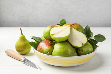 Fresh ripe pears, knife and green leaves on white wooden table, closeup