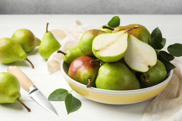 Fresh ripe pears, knife and green leaves on white wooden table, closeup