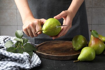 Woman cutting fresh ripe pear at black table, closeup