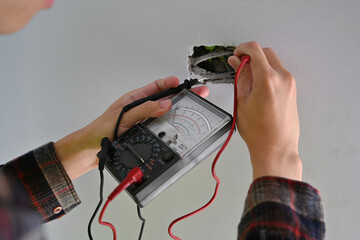 Hands of an electrician holding a multimeter and probes while inspecting home electrical connections
