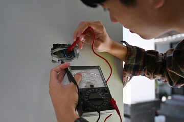 Close-up of electrician using a multimeter to check electrical wiring inside a wall socket during installation or repair