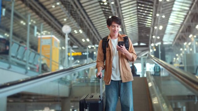Happy asian man with backpack checking flight in phone on escalator in airport terminal, People concentrating typing digital device for travel in transportation, Concept of travel