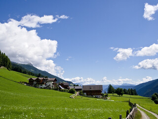 Scenic alpine countryside in Italy with meadows and traditional homes.