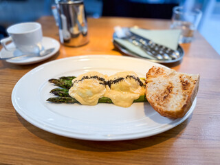 Eggs benedict with asparagus and toast served on white plate. Breakfast, gastronomy, indulgence, and cafe lifestyle.