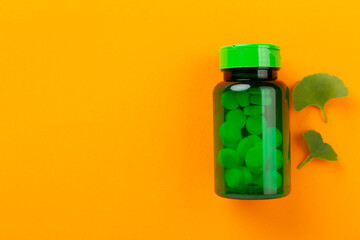 Ginkgo leaf with bottle of pills on color background, top view