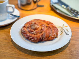 Sweet cinnamon pastry served on white plate in cafe. Dessert, indulgence, appetite, and morning lifestyle.