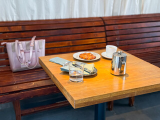 Coffee and pastry on wooden table next to pink bag. Breakfast, indulgence, and social cafe lifestyle.