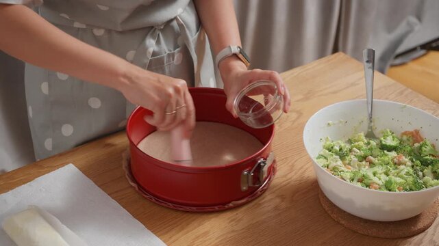 Greasing a red baking pan with melted butter or oil. A woman uses a pastry brush to prepare a non-stick surface on bakeware before baking a homemade cake, pie, or puff pastry tart.