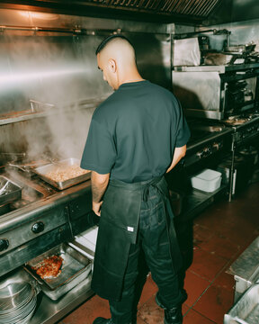A man in a black apron stands by the stove in the kitchen. The atmosphere of modern fast food in the kitchen.