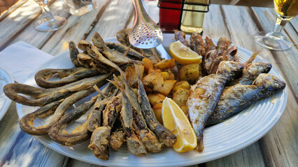 Seafood platter with potatoes and lemon on a white plate. Assortment of different fish on a platter on a wooden table. Tasty and healthy food. Assortment of fried sea fish with potatoes