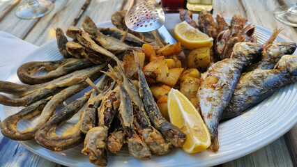 Seafood platter with potatoes and lemon on a white plate. Assortment of different fish on a platter on a wooden table. Tasty and healthy food. Assortment of fried sea fish with potatoes