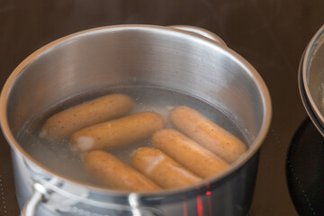 Small sausages are heated in water in a pot on the stove