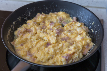 Scrambled eggs with salami in a large frying pan