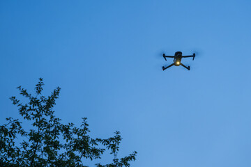 Close-up of a small glowing drone hovering in the evening.
