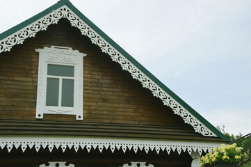Triangular roof of brown wooden house with white decorative carved decoration.