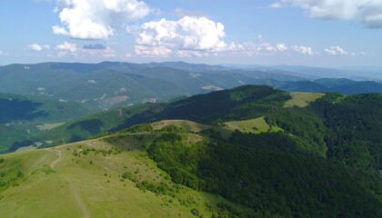 Obraz premium A sweeping vista reveals rolling hills and dense forests, showcasing a picturesque mountain landscape under a bright, sunny sky.