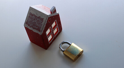 A closed lock without a key lies in front of a small house figurine. Traditional padlock to protect your own home from burglary
