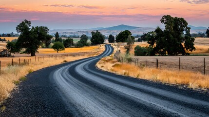 Fototapeta premium A winding country road stretches through golden fields at sunrise, painting a tranquil scene of rural beauty.