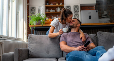Obraz premium Woman bringing coffee to partner in living room. Man relaxing on grey sofa during morning hours, enjoying morning routine.