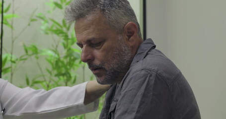 Fototapeta premium Close-up of middle-aged male patient reacting to difficult diagnosis during consultation, emotional response while being supported by doctor in clinical setting