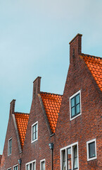 Obraz premium The bright orange rooftops of three traditional row houses in Naarden, a historic fortified town in the Netherlands, showcasing Dutch brick architecture and charming gabled facades