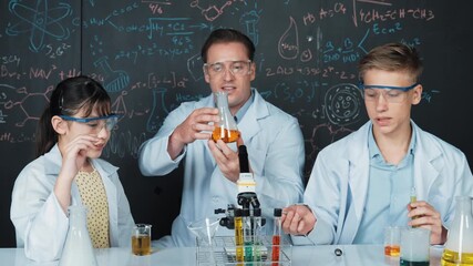 Smart girl inspect colored liquid while diverse student doing experiment in STEM science class. Group of high school children working in laboratory while standing at blackboard. Creative. Edification - Powered by Adobe