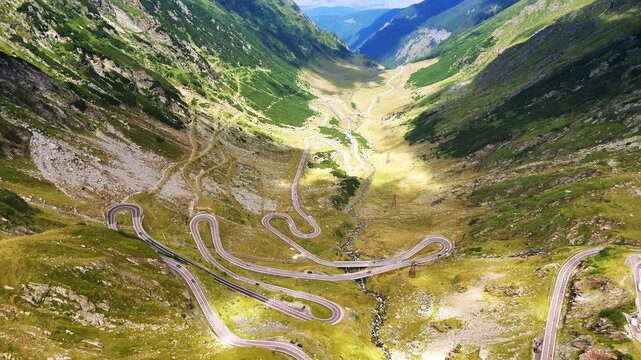 Cars run by the wavy highway on the mountains slopes. Drone footage over the picturesque road Transfagarash in Romania.
