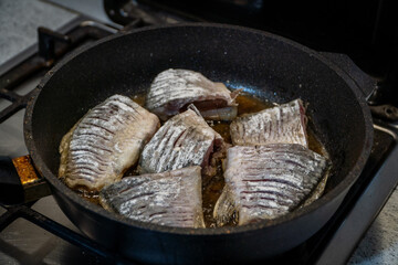 Fried crucian fish in a frying pan top view, close-up. Pieces of large fish in batter are fried in a frying pan in oil. Cooking fish in the home kitchen, deep fried fishes high-calorie food. 