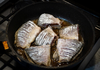 Fried crucian fish in a frying pan top view, close-up. Pieces of large fish in batter are fried in a frying pan in oil. Cooking fish in the home kitchen, deep fried fishes high-calorie food. 