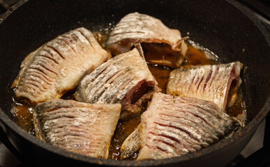 Fried crucian fish in a frying pan top view, close-up. Pieces of large fish in batter are fried in a frying pan in oil. Cooking fish in the home kitchen, deep fried fishes high-calorie food. 