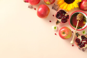 Flat lay of apples, pomegranates, honey, and sunflower on peach background. Rosh Hashanah celebration concept.