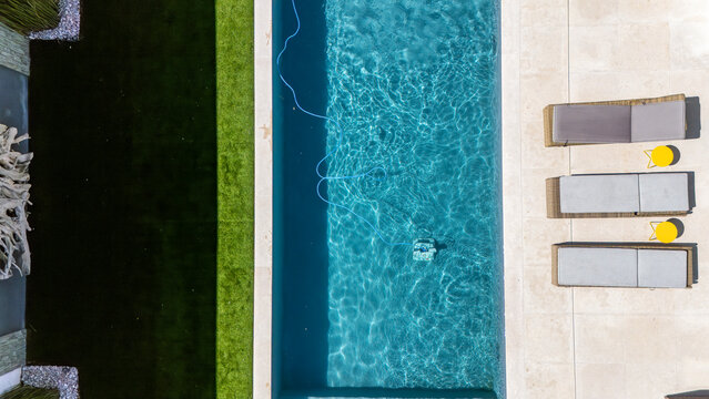 Piscine contemporaine int&eacute;gr&eacute;e dans un jardin moderne avec pelouse soign&eacute;e et am&eacute;nagement paysager &eacute;l&eacute;gant. Vue sur un robot qui nettoie la piscine.