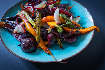 Grilled carrots, beets, asparagus, and onions on a blue plate.