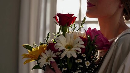 A close-up video captures a woman holding a vibrant bouquet of flowers, with soft lighting and a side profile angle highlighting her serene expression.