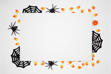 Halloween frame of scattered candy and decor surrounding white paper with copy space. Top view over a white background.
