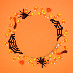 Halloween circle frame of scattered candy and decor surrounding orange paper with copy space. Above view over a orange background.