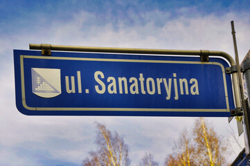 Ustroń Zawodzie – słynne piramidy. Zdjęcie niebieskiego znaku ulicy Sanatoryjnej na tle czystego nieba i widocznych gałęzi.  © Pol Badger