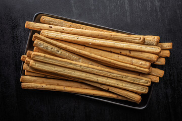 Crispy grissini breadsticks on plate on black table. Top view.