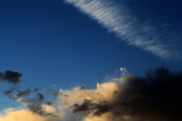 A dramatic sky, with dark clouds contrasting against a wispy contrail