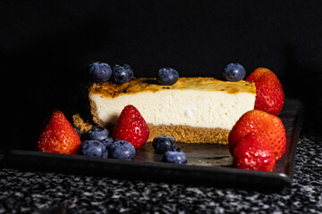 A piece of cheesecake with fruits on a dark background
