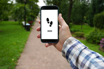 Man checking daily steps counter on smartphone in park: reaching fitness goal