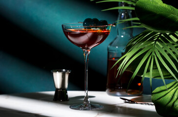 Rob Roy alcoholic cocktail with whiskey, red vermouth, bitters and cocktail cherry. Marble table, elegant background with green plants