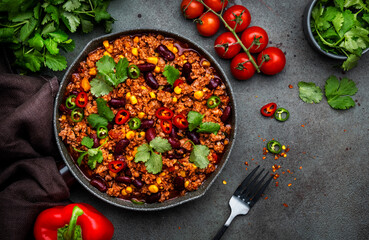 Chili con carne with beef, beans, paprika, corn, cilantro, jalapeno in tomato sauce, in frying pan, rusty green background top view