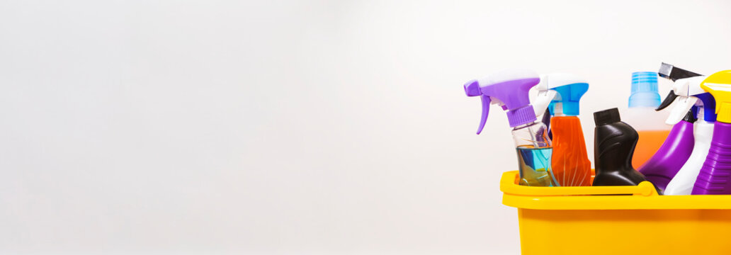 Bright multi-colored cleaning products, household chemicals bottles and sprays, rags, sponges in orange bucket for washing, wiping and dusting - Powered by Adobe