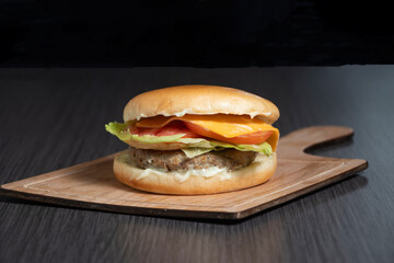 Delicious crispy chicken burger with melted cheese, fresh lettuce and tomato on wooden board side view of fast food