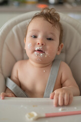 Fototapeta na wymiar Cute baby boy smeared in sour cream sits in a high chair. 