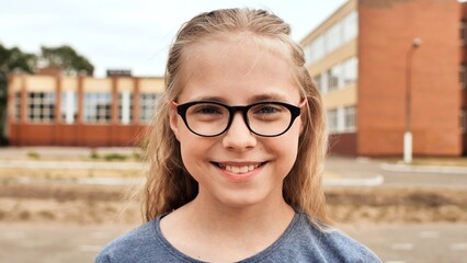 Cheerful female student wearing glasses, beaming with enthusiasm near school entrance, embodying academic excitement